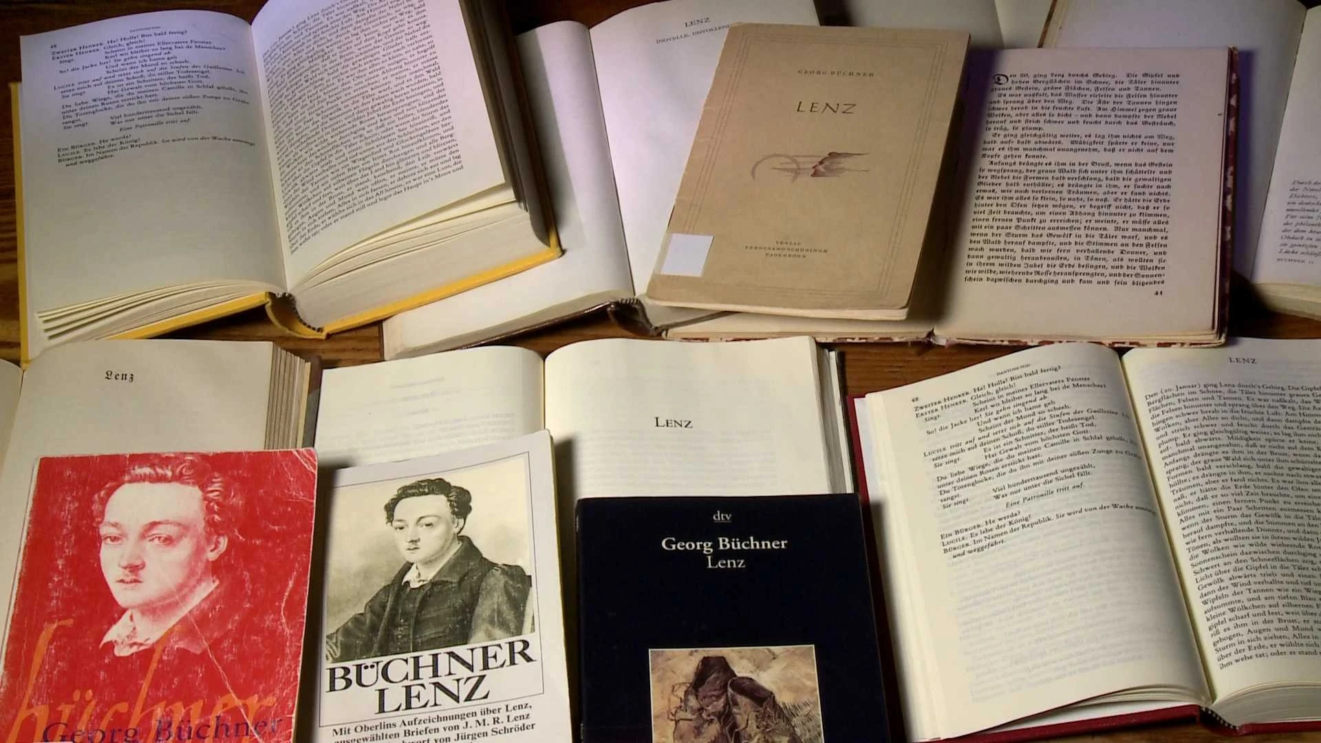 Auf einer Fläche sind mehrere aufgeschlagene und geschlossene Bücher ausgestellt, die auf mehreren Einbänden und Seiten den Titel Lenz und Porträts von Georg Büchner zeigen.