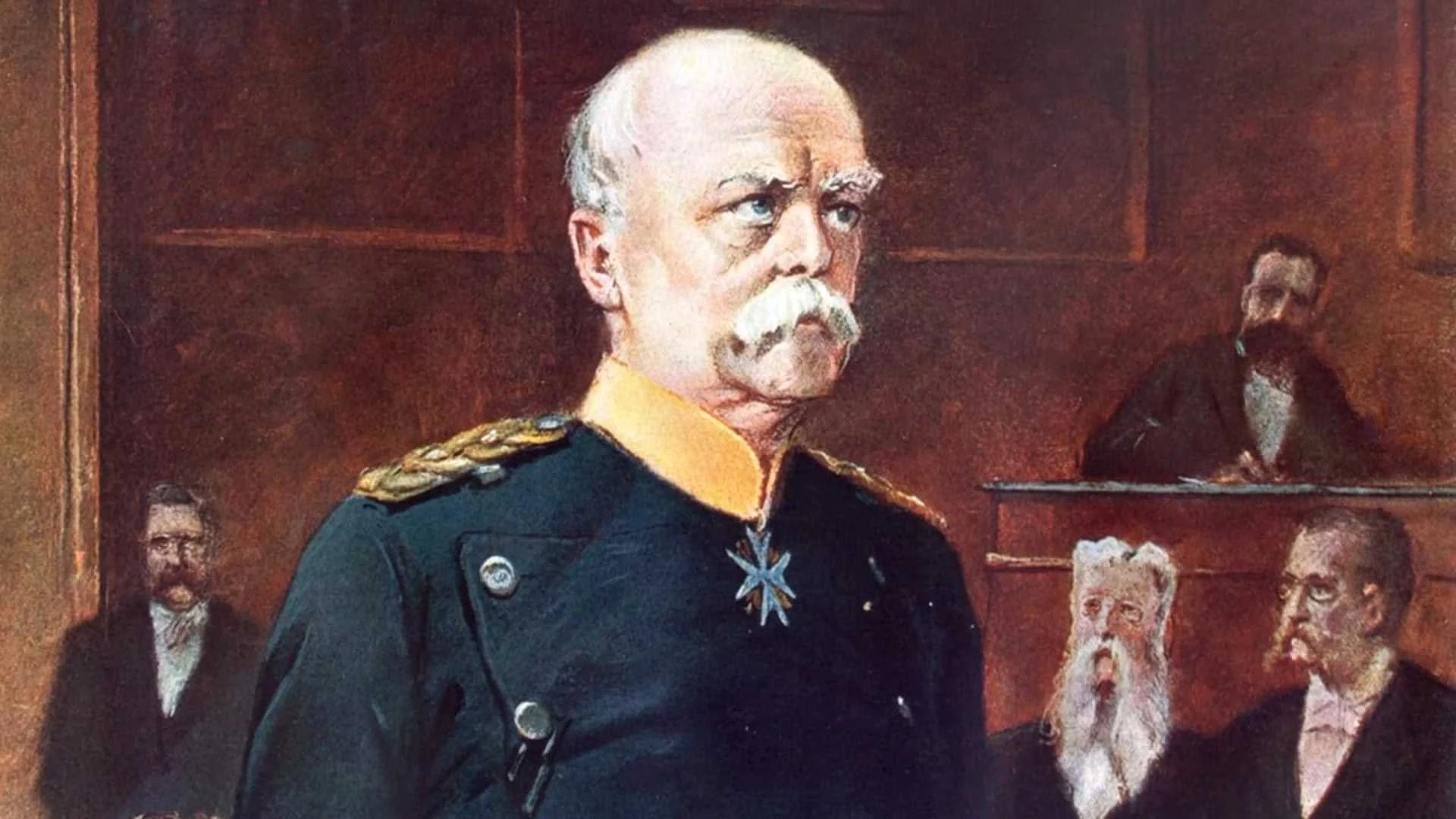 Ein strenger Mann in einer dekorierten Militäruniform steht in einem formellen Raum, in dem mehrere Männer sitzen und beobachten.