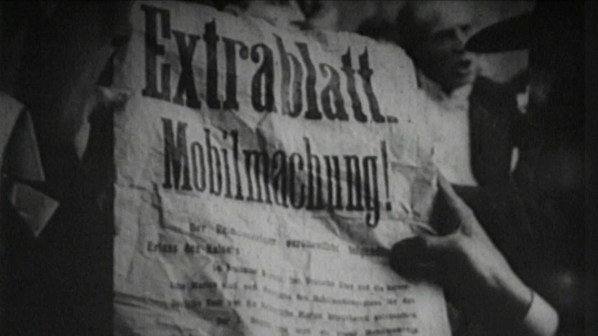 Eine Person hält eine zerknitterte Zeitung mit der Schlagzeile Extrablatt Mobilmachung! umgeben von Menschen im Hintergrund.