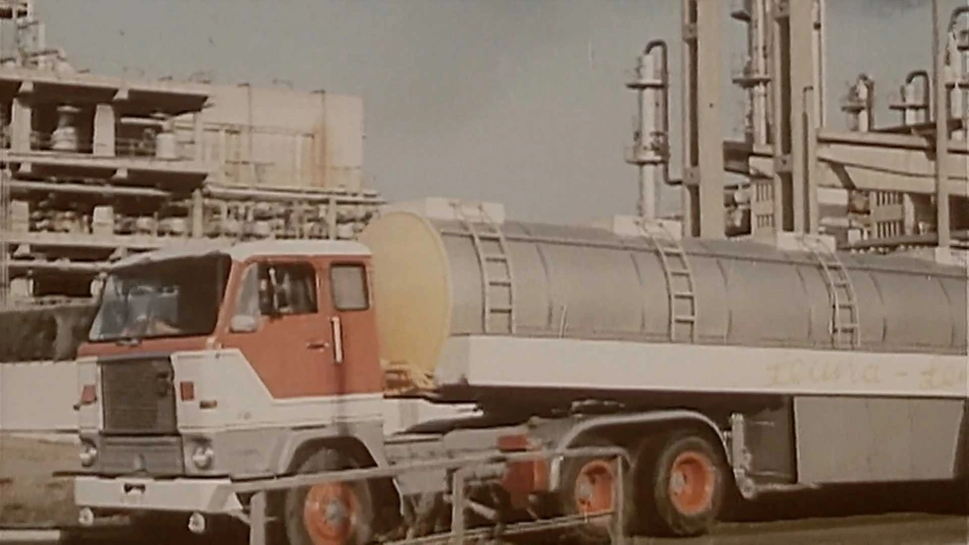 Ein rot-weißer Tankwagen parkt in der Nähe von Industrieanlagen mit Rohren und Lagertanks im Hintergrund.