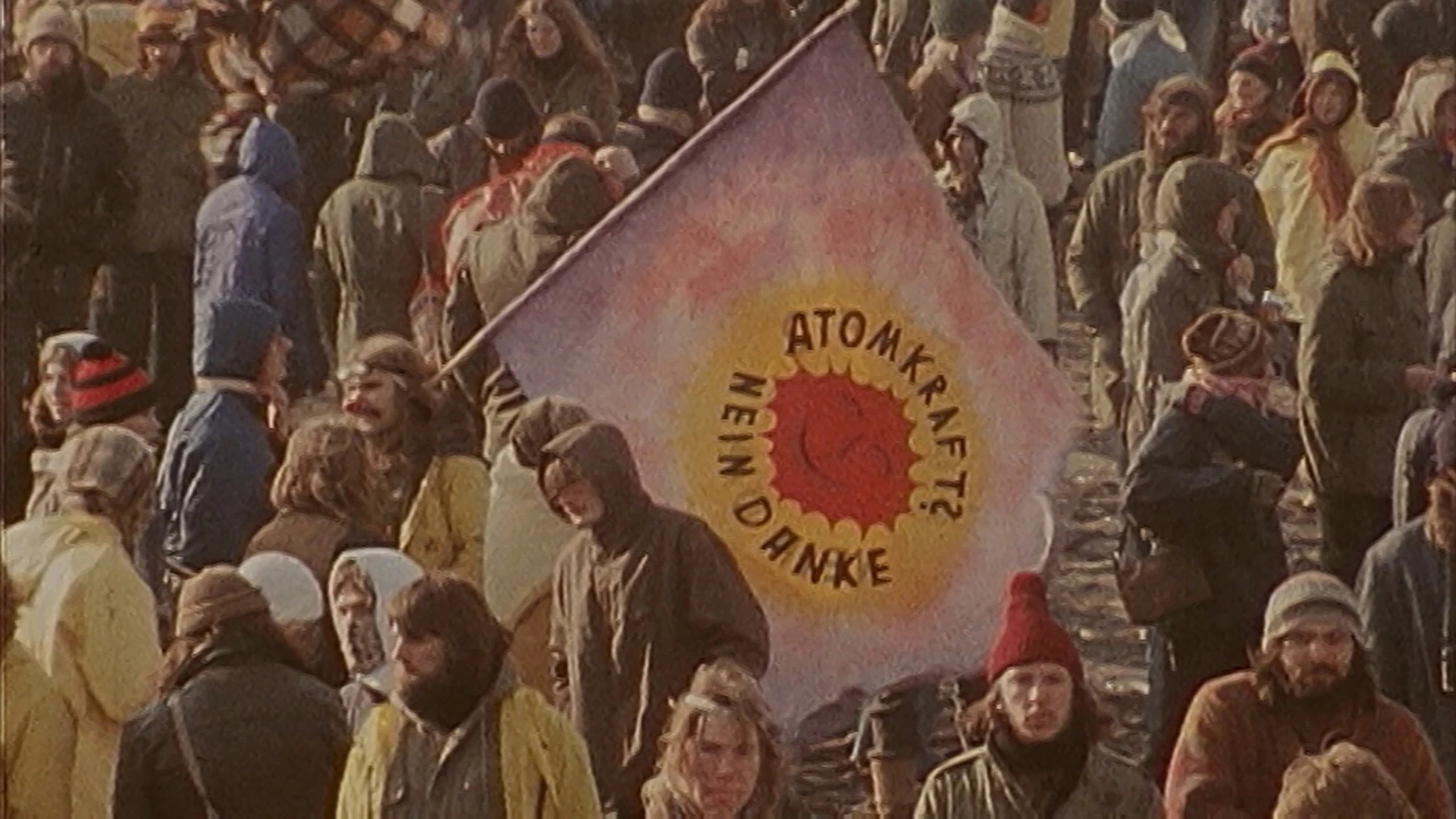 Eine Menschenmenge im Freien hält eine Fahne mit einer roten Sonne und dem Schriftzug "Atomkraft? Nein Danke", was so viel heißt wie "Atomkraft? Nein Danke.".
