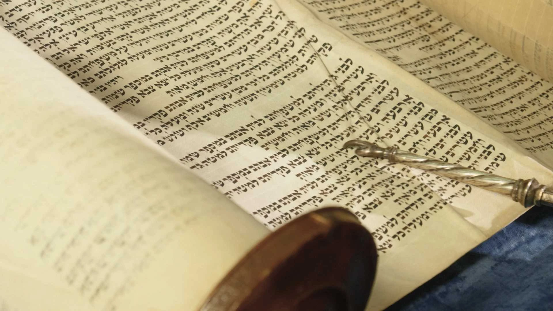 Eine Tora-Rolle mit hebräischem Text ist teilweise entrollt, ein silberner Yad-Zeiger liegt auf dem Pergament.