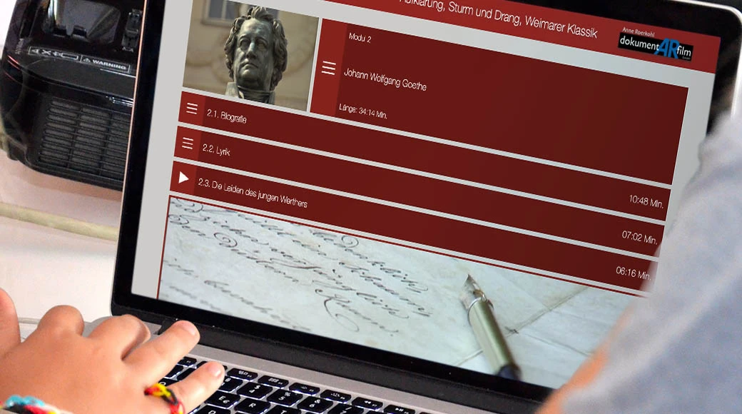 Eine Person, die einen Laptop benutzt, der einen Videovortrag über Johann Wolfgang Goethe zeigt, mit einem Menü von Videothemen und -dauer auf dem Bildschirm.